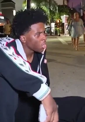 Nitro Camden reacting while seated on a city sidewalk during a nighttime IRL stream.